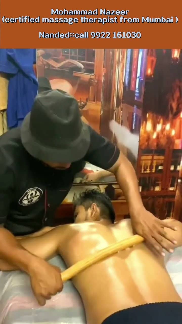 A therapist in the centre's black uniform working a long wooden stick along a client's oiled back on the treatment table.