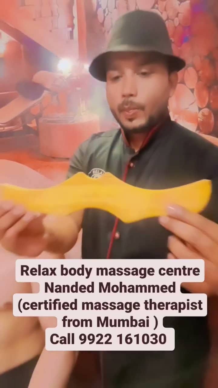 A therapist holding up a shaped yellow wooden massage tool to the camera in the treatment room.